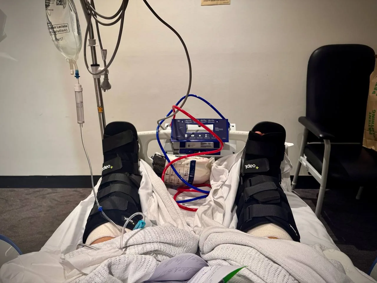 Hospital bed view: both legs in surgical boots, IV line running.