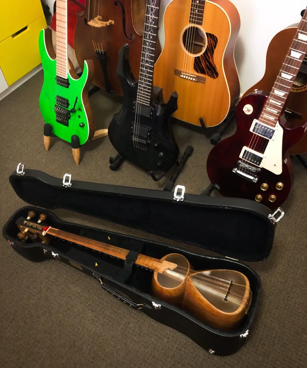A saz in an open case in front of electric and acoustic guitars.