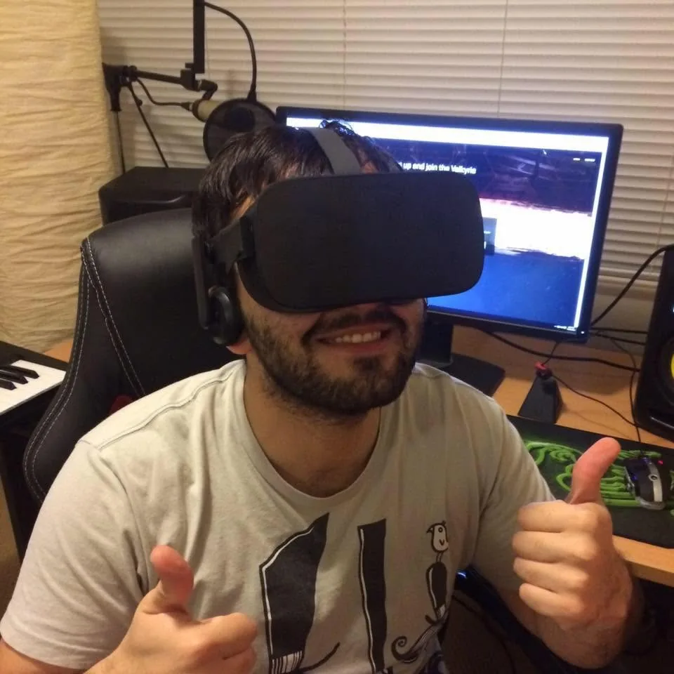 Thumbs up in a VR headset at a cluttered desk.