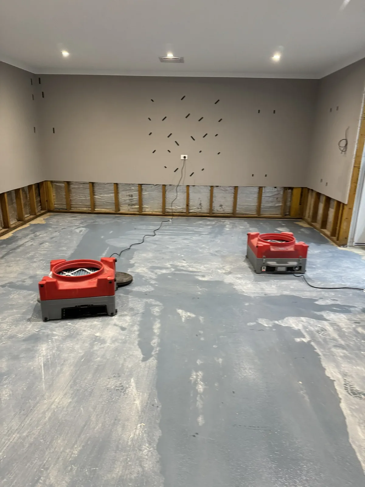 A gutted room with stripped walls and two air movers on bare concrete.