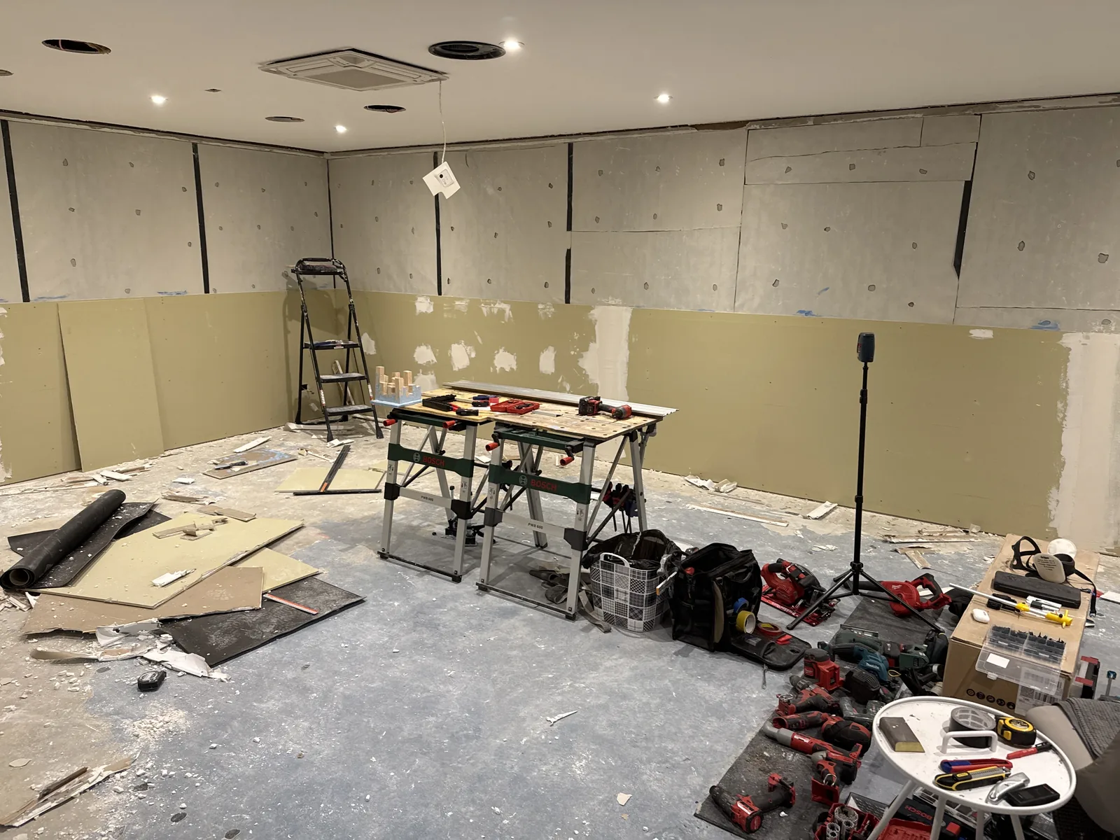 A room mid-replaster: workbenches, ladder, tools everywhere.