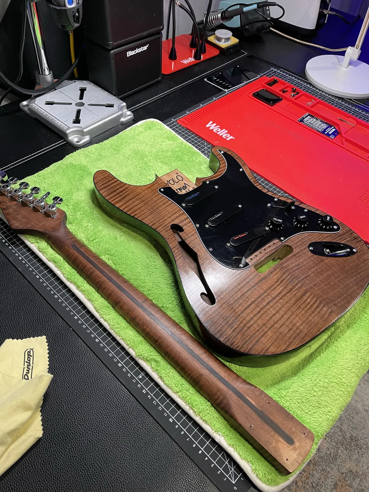 A rosewood guitar body and neck laid out on a green mat.