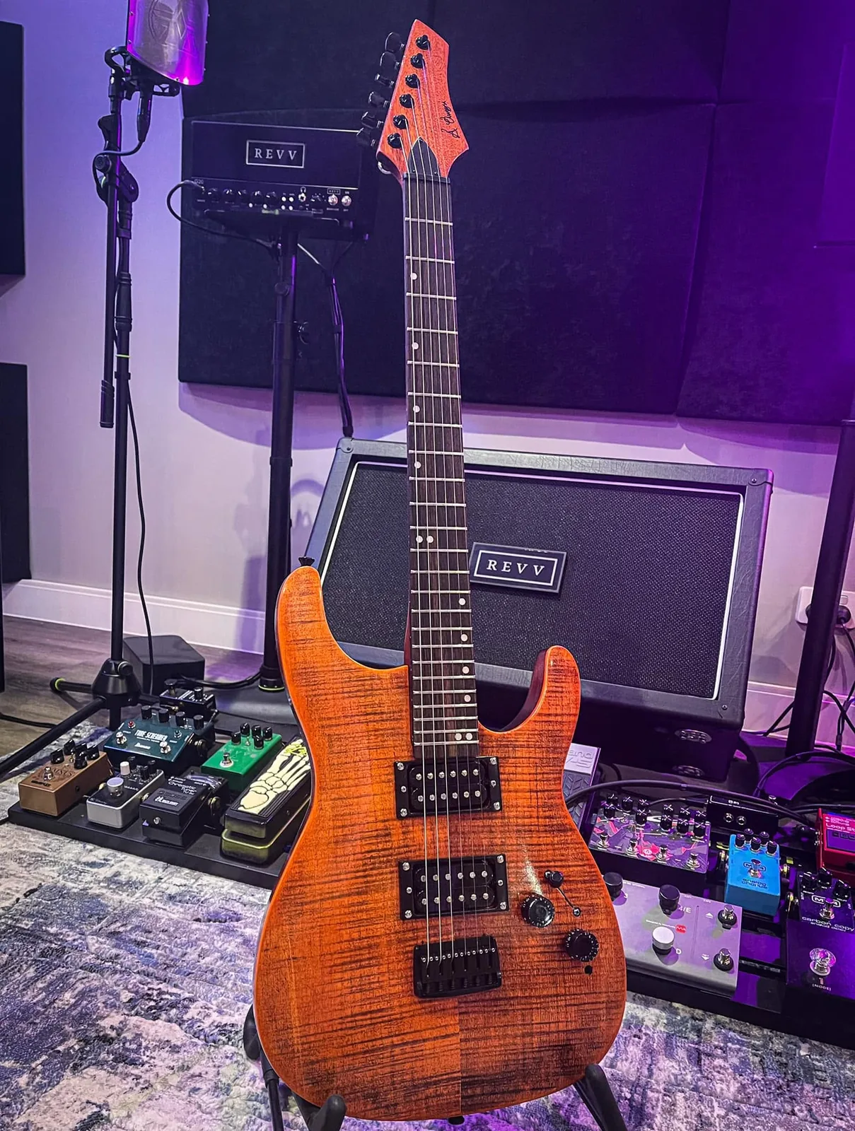 An orange flame-maple superstrat in front of amps.