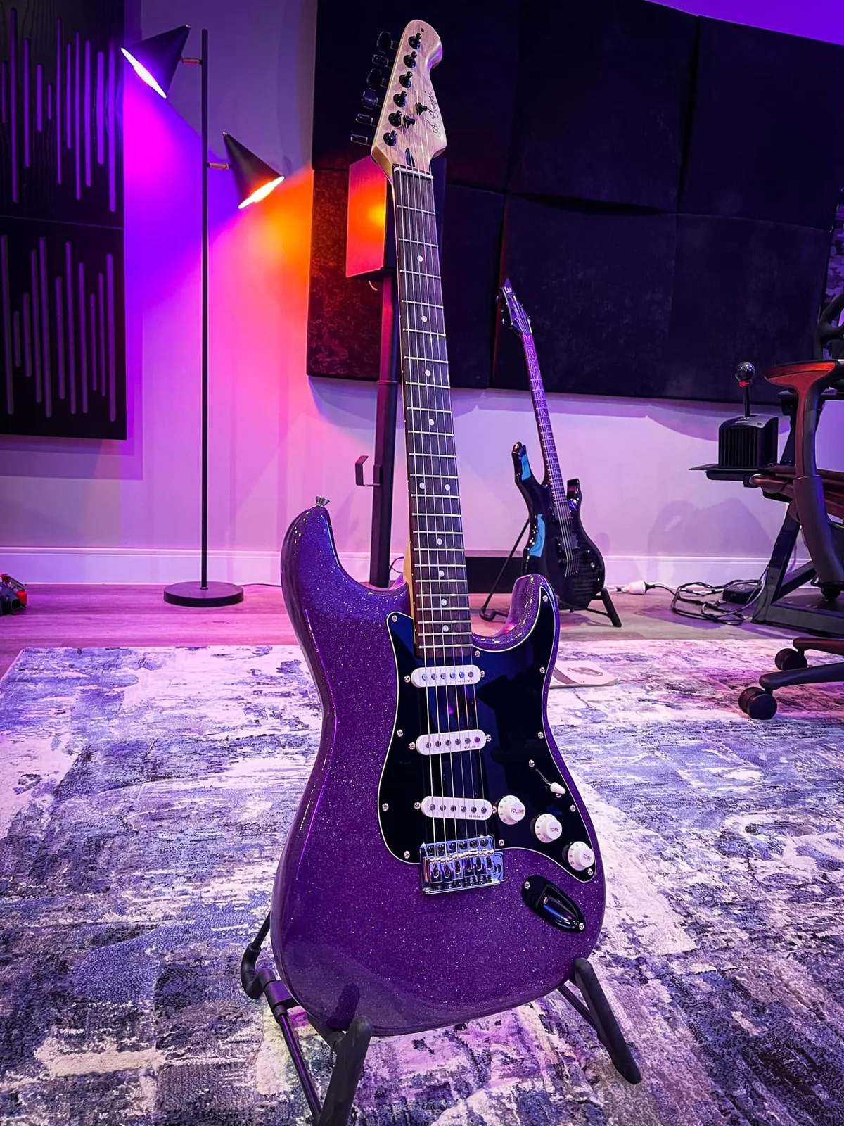 A purple sparkle strat-style guitar on a stand.