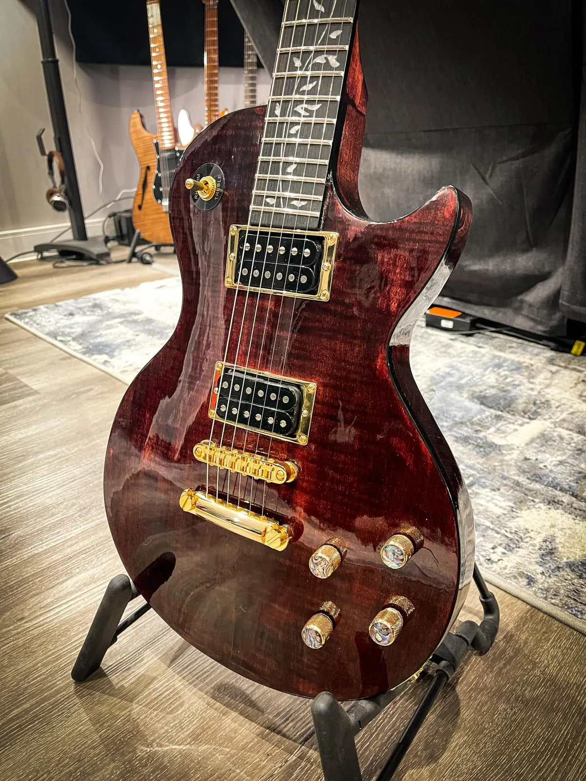A wine-red Les Paul with gold hardware on a stand.